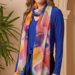 Woman wearing a colorful scarf and blue top indoors with a plant in the background