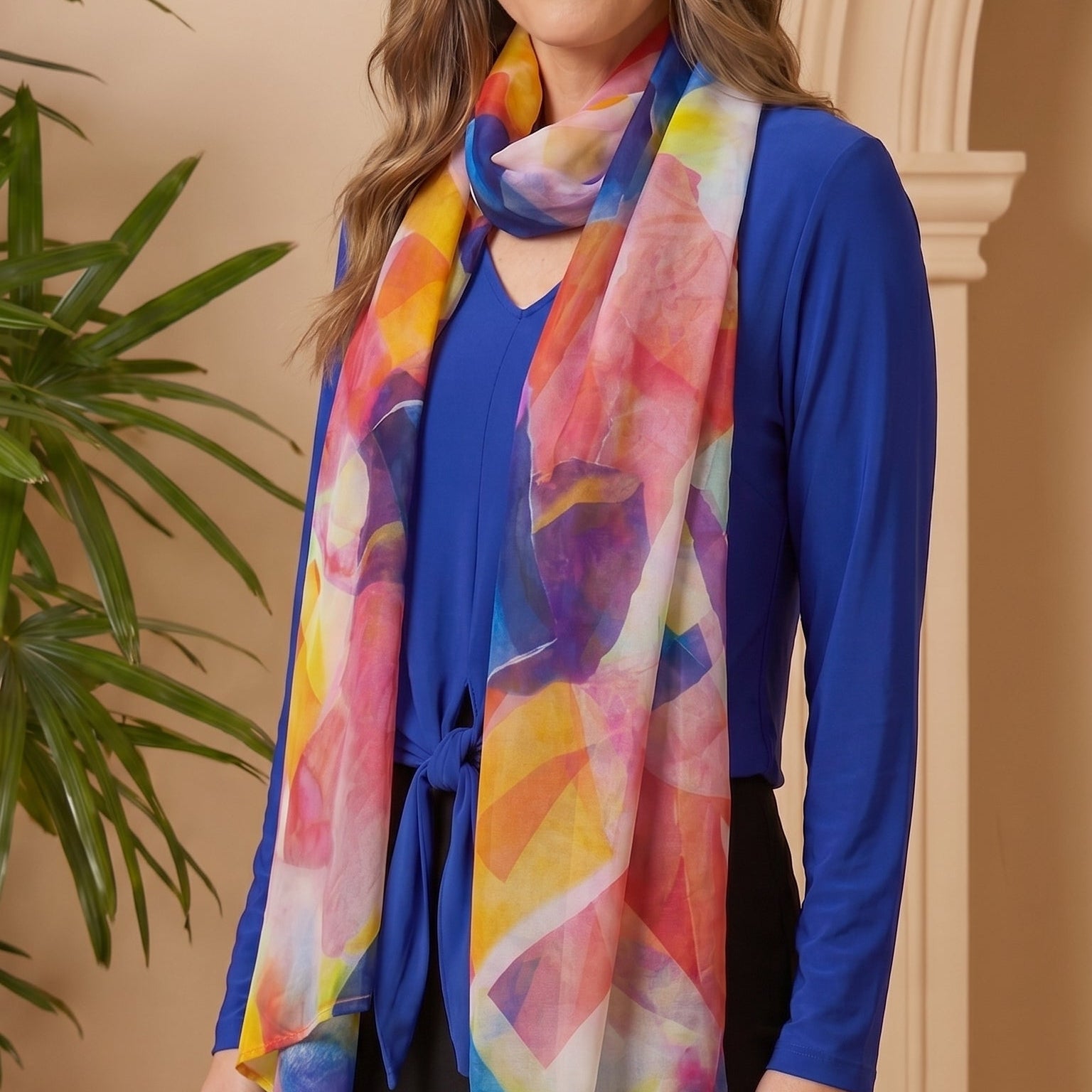 Woman wearing a colorful scarf and blue top indoors with a plant in the background