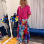 Woman wearing pink short sleeve top and colourful skirt.