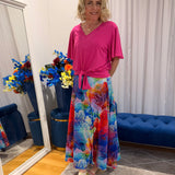 Woman wearing pink short sleeve top and colourful skirt.