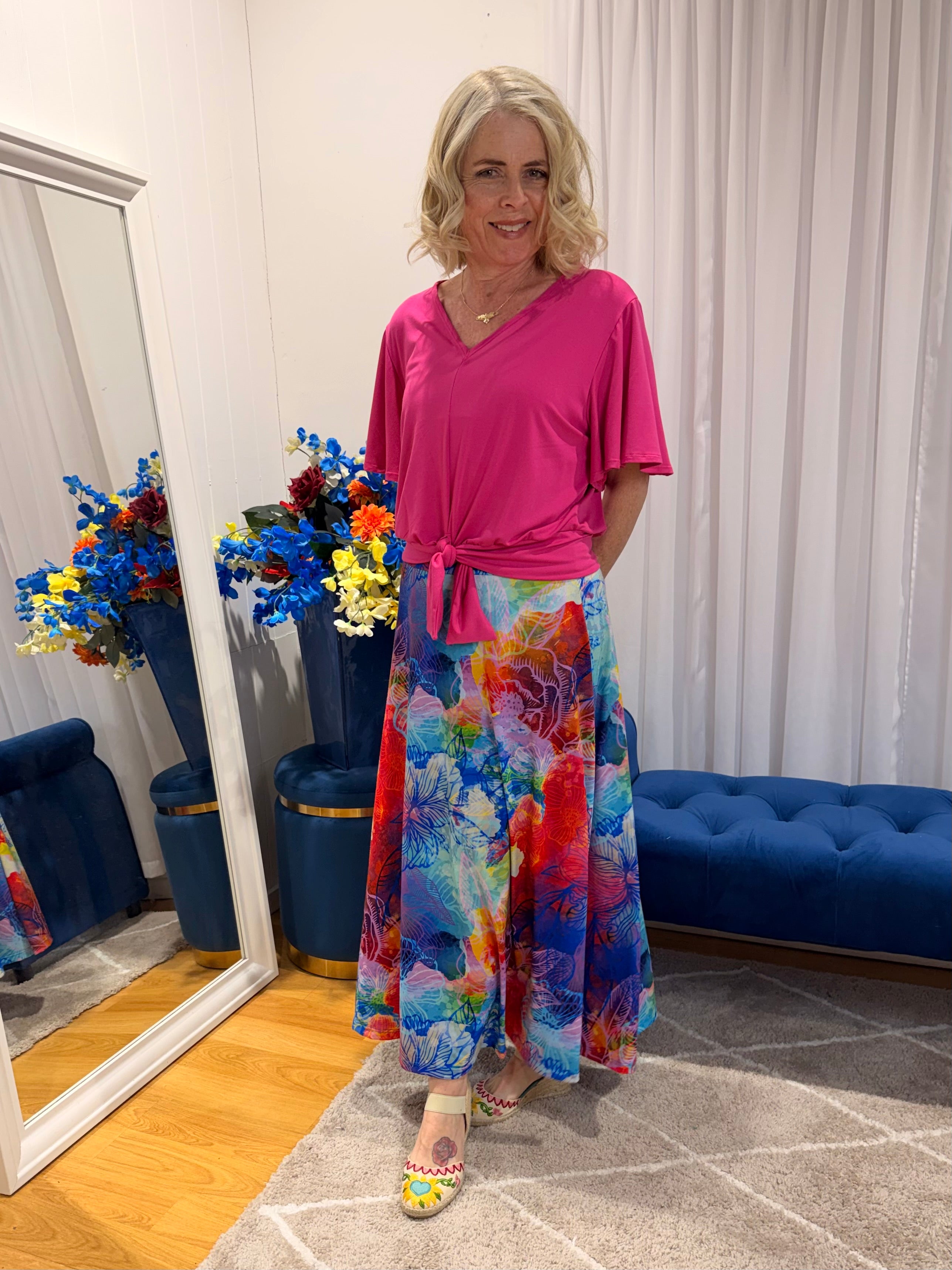Woman wearing pink short sleeve top and colourful skirt.