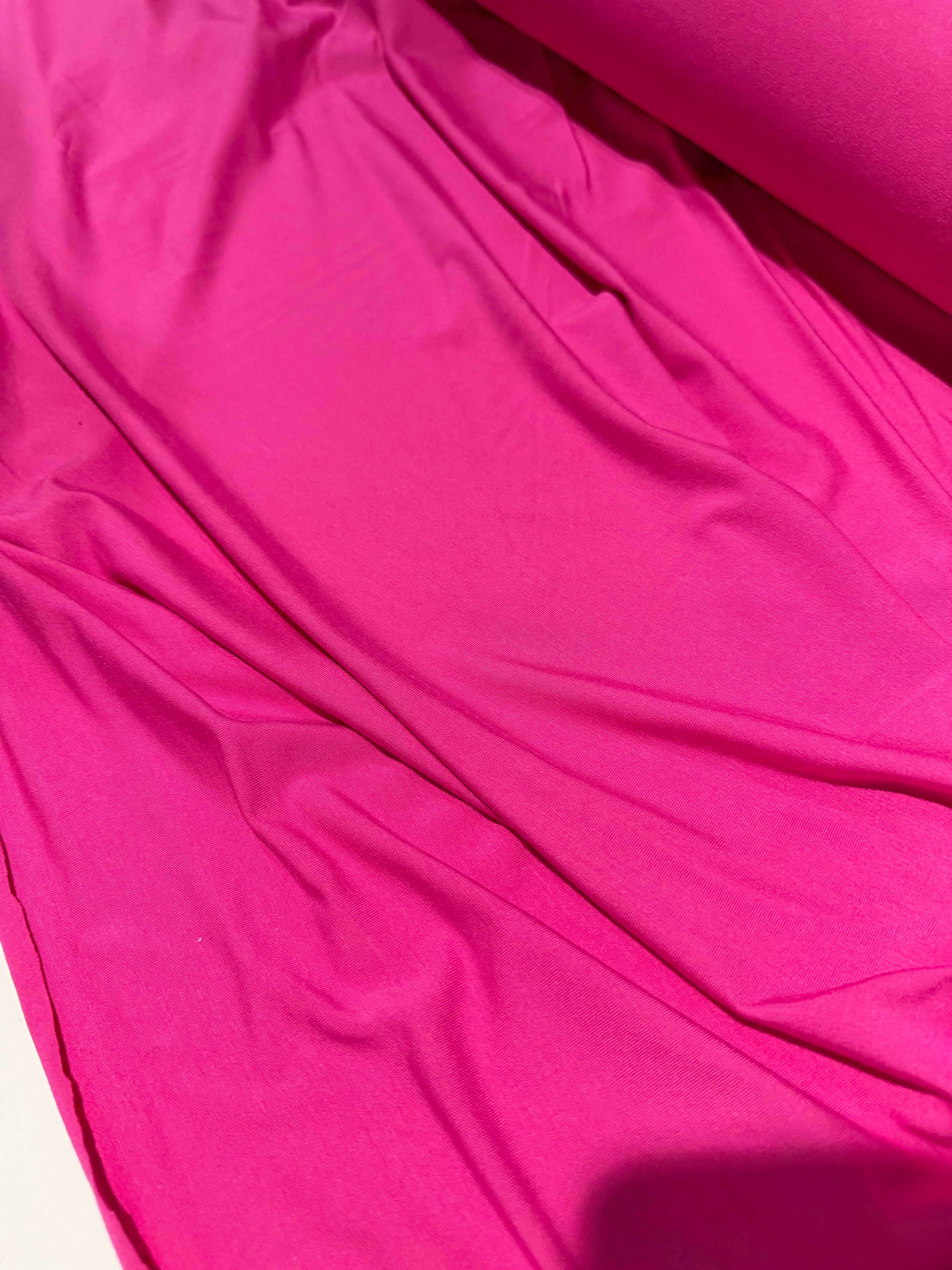 Bright pink fabric draped in soft folds, showing a smooth texture and solid color.
