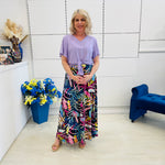 Woman in a colorful long skirt and top  standing in a room with decorative elements.