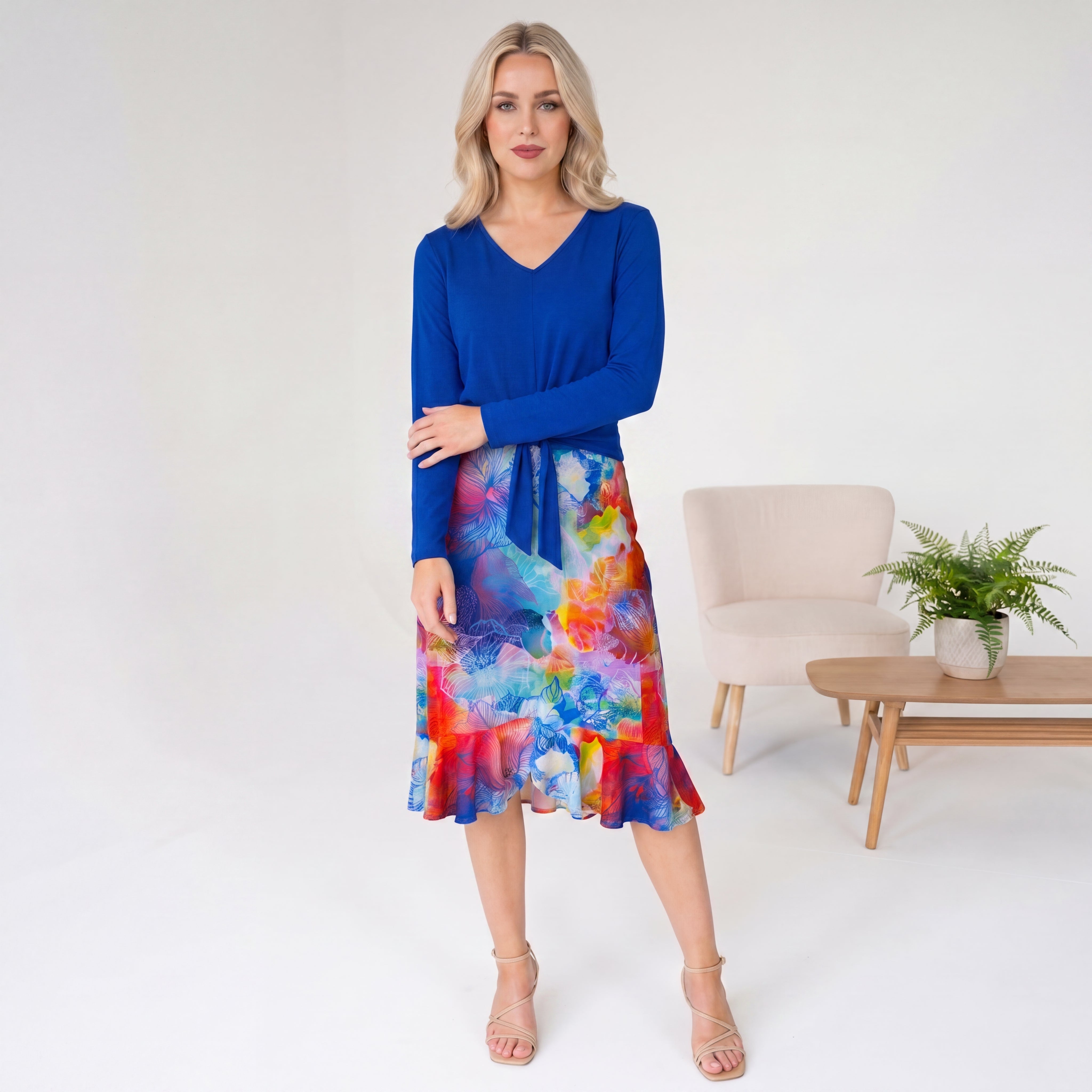 Woman wearing a blue top and colorful skirt in a minimalistic room.