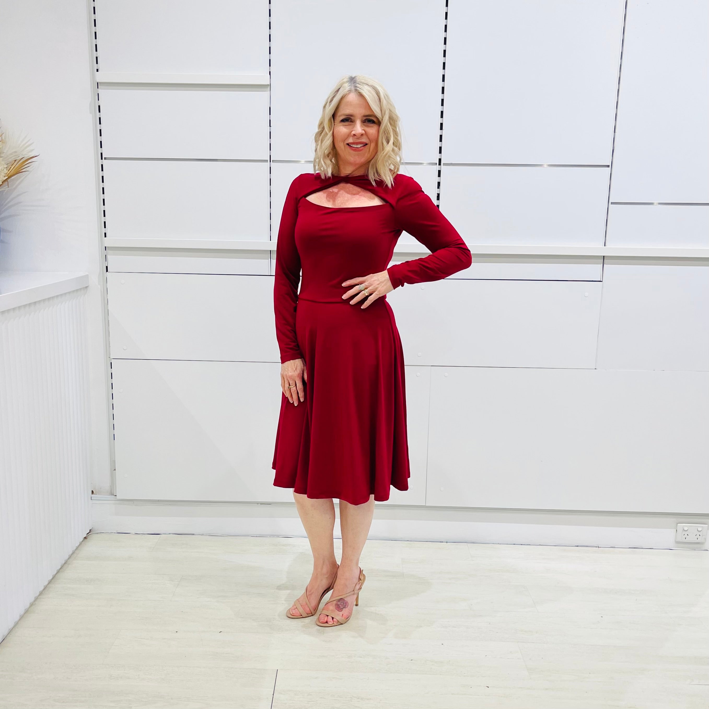 Woman wearing the Penelope dress n rich ruby red, featuring a fit-and-flare, knee length, slihouette, full length sleeves, and a cut out neckline.