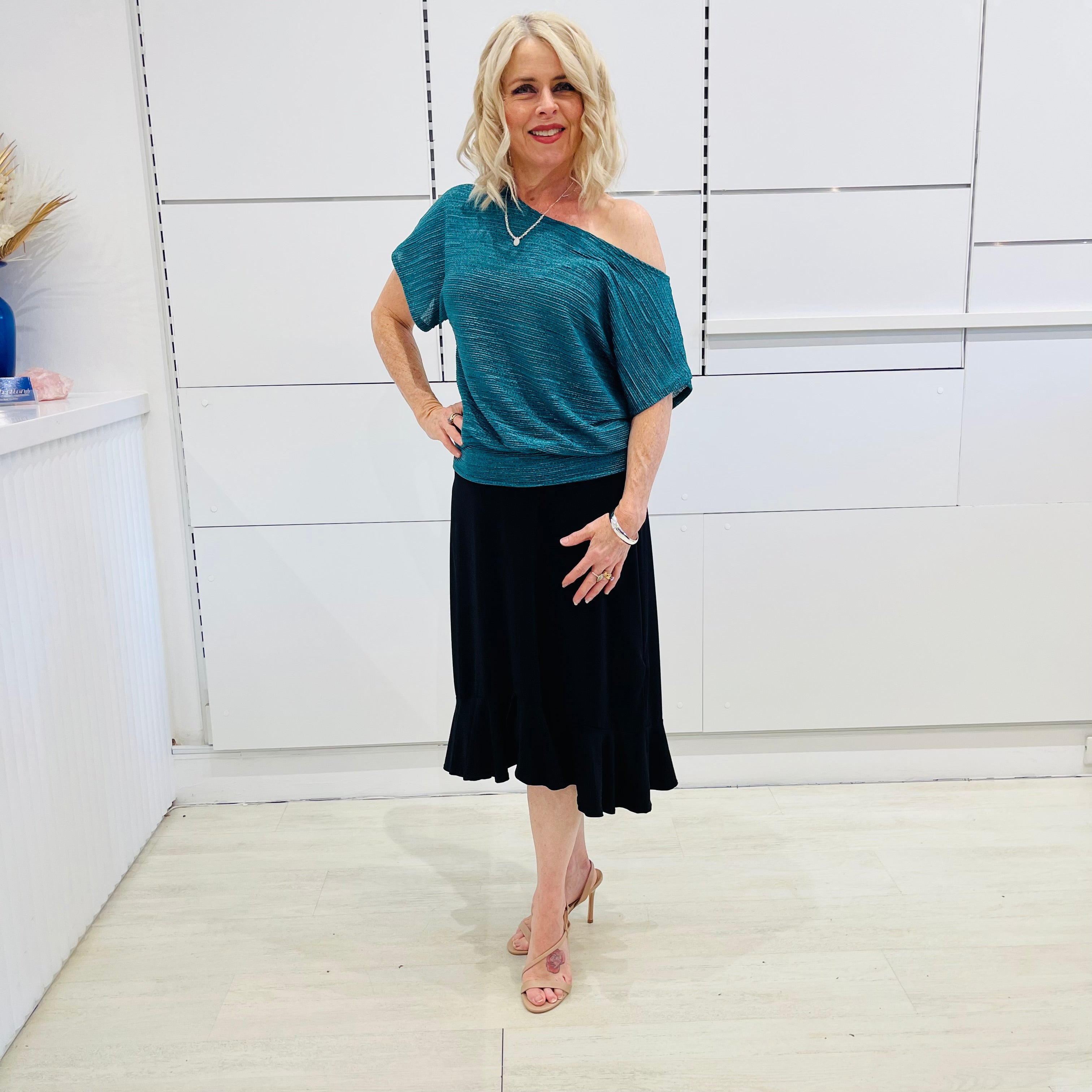 Stunning off the shoulder emerald green top with delicate shimmer. Flattering relaxed fit cut with stretch waistband for style and fit. Worn with black stretch skirt with asymmetrical hemline small ruffle detail.