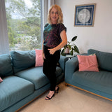 Woman standing in a living room with blue sofas and pink cushions.