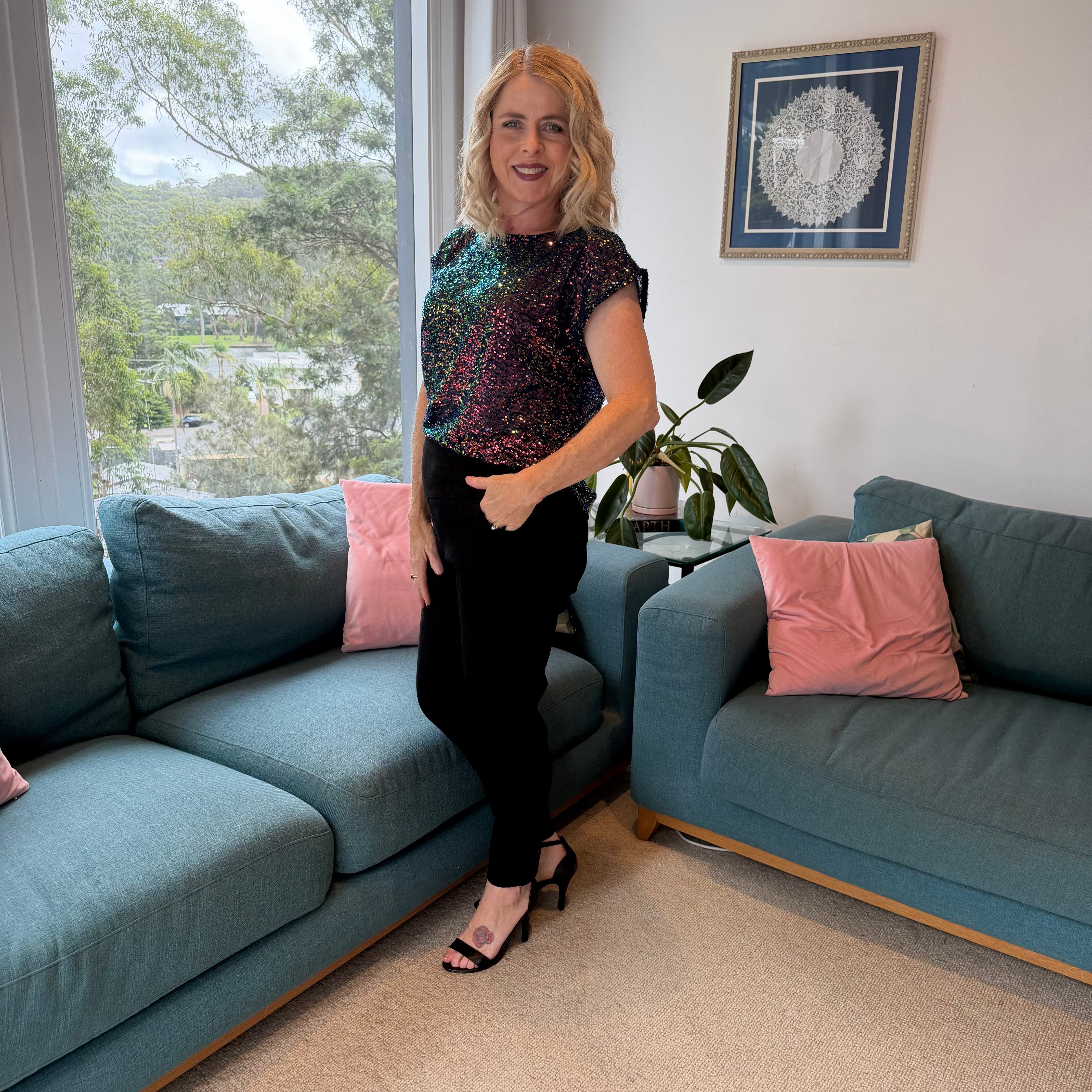 Woman standing in a living room with blue sofas and pink cushions.