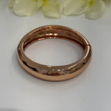 Rose gold bracelet on a white surface with light green flowers in the background