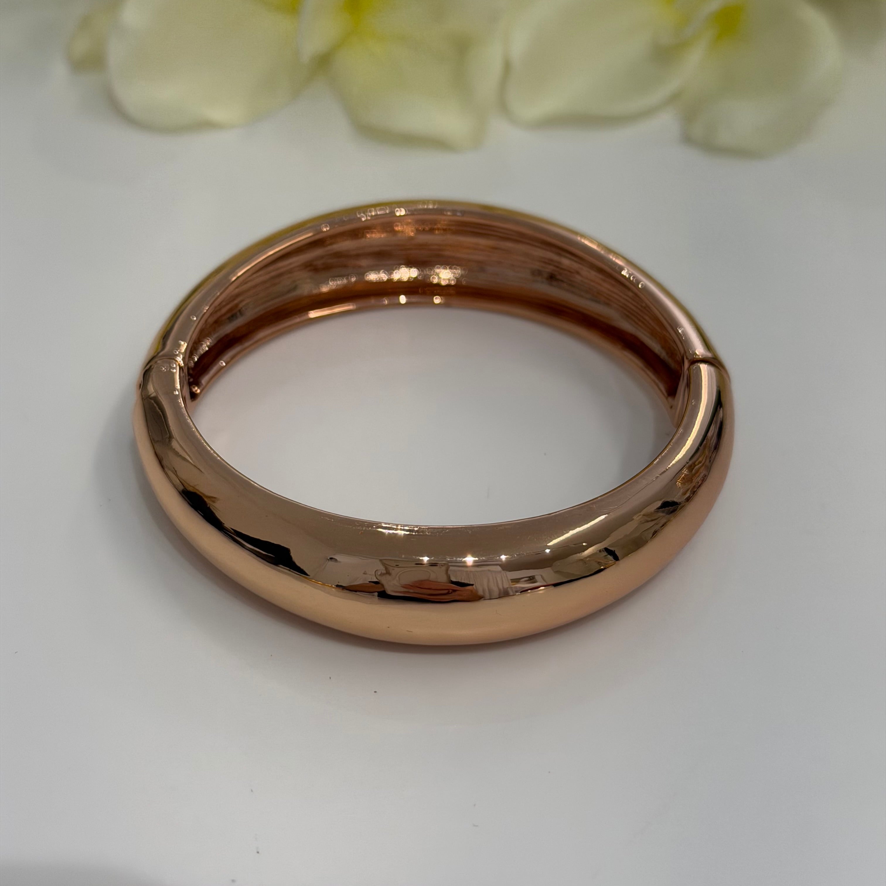 Rose gold bracelet on a white surface with light green flowers in the background