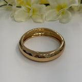 Gold bangle on a white surface with flowers in the background