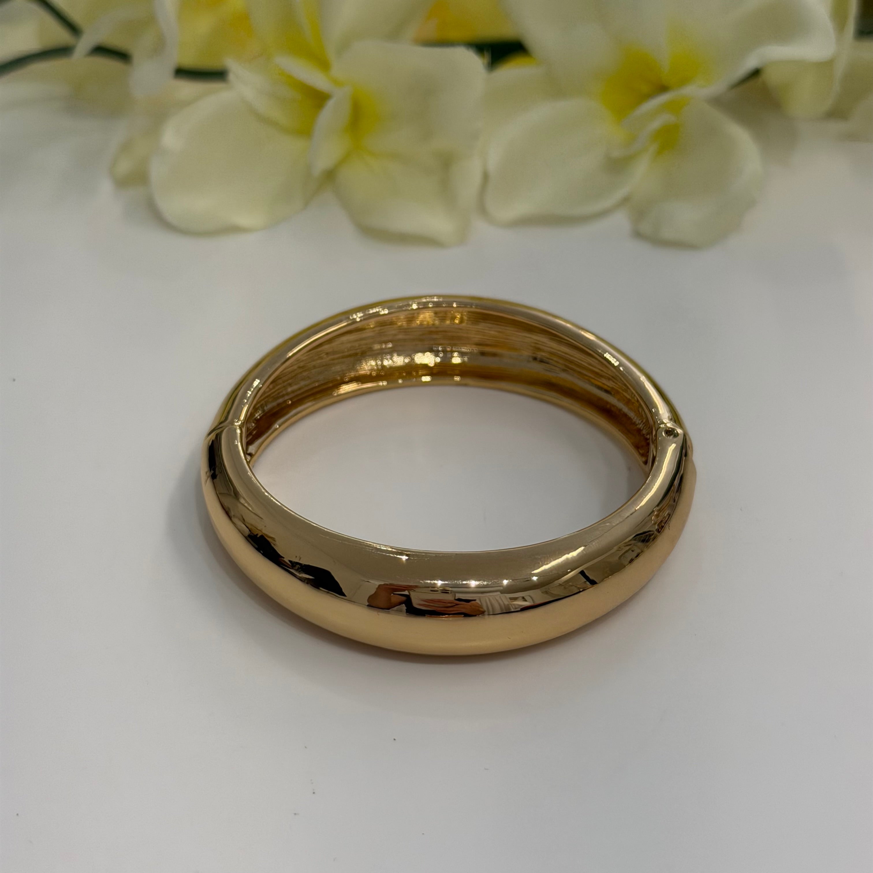 Gold bangle on a white surface with flowers in the background