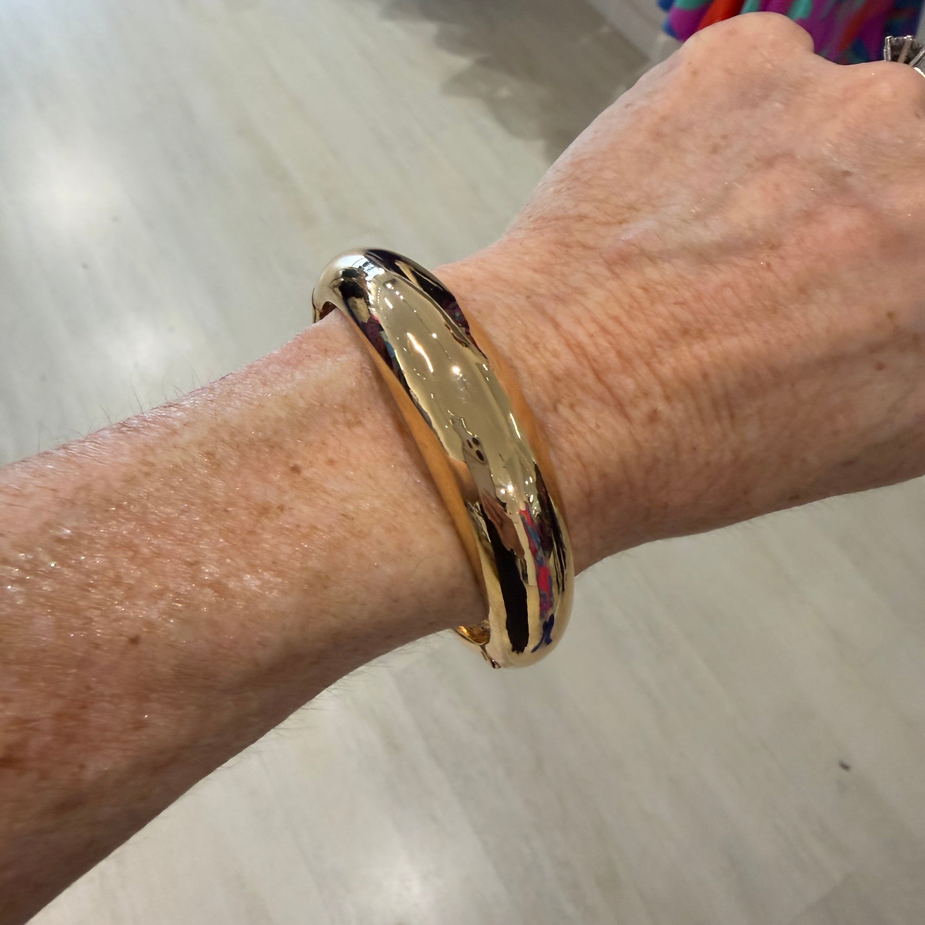 Gold bracelet on a wrist with a neutral background