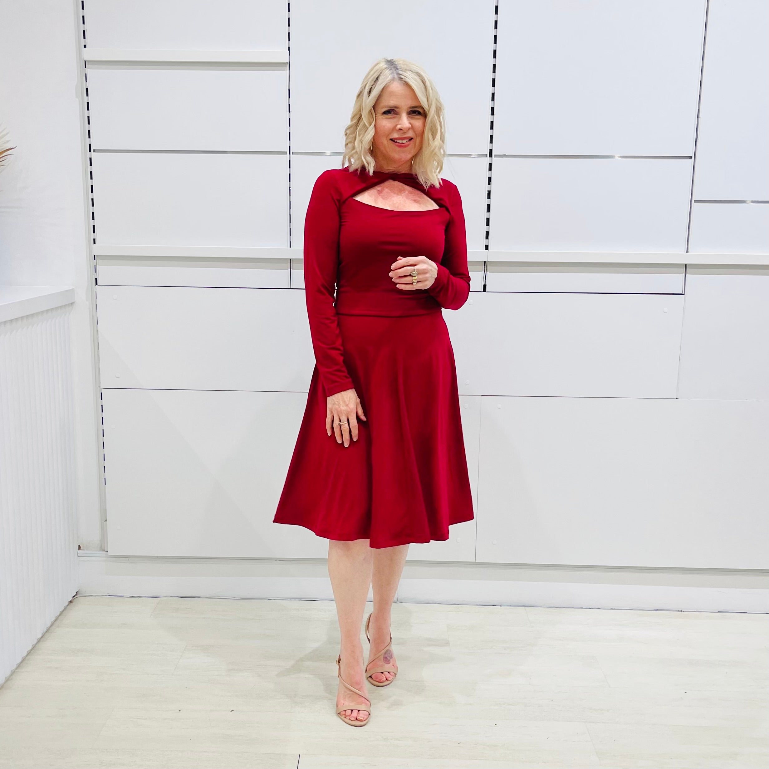 Woman wearing the Penelope dress n rich ruby red, featuring a fit-and-flare, knee length, slihouette, full length sleeves, and a cut out neckline.
