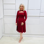 Woman wearing the Penelope dress n rich ruby red, featuring a fit-and-flare, knee length, slihouette, full length sleeves, and a cut out neckline.