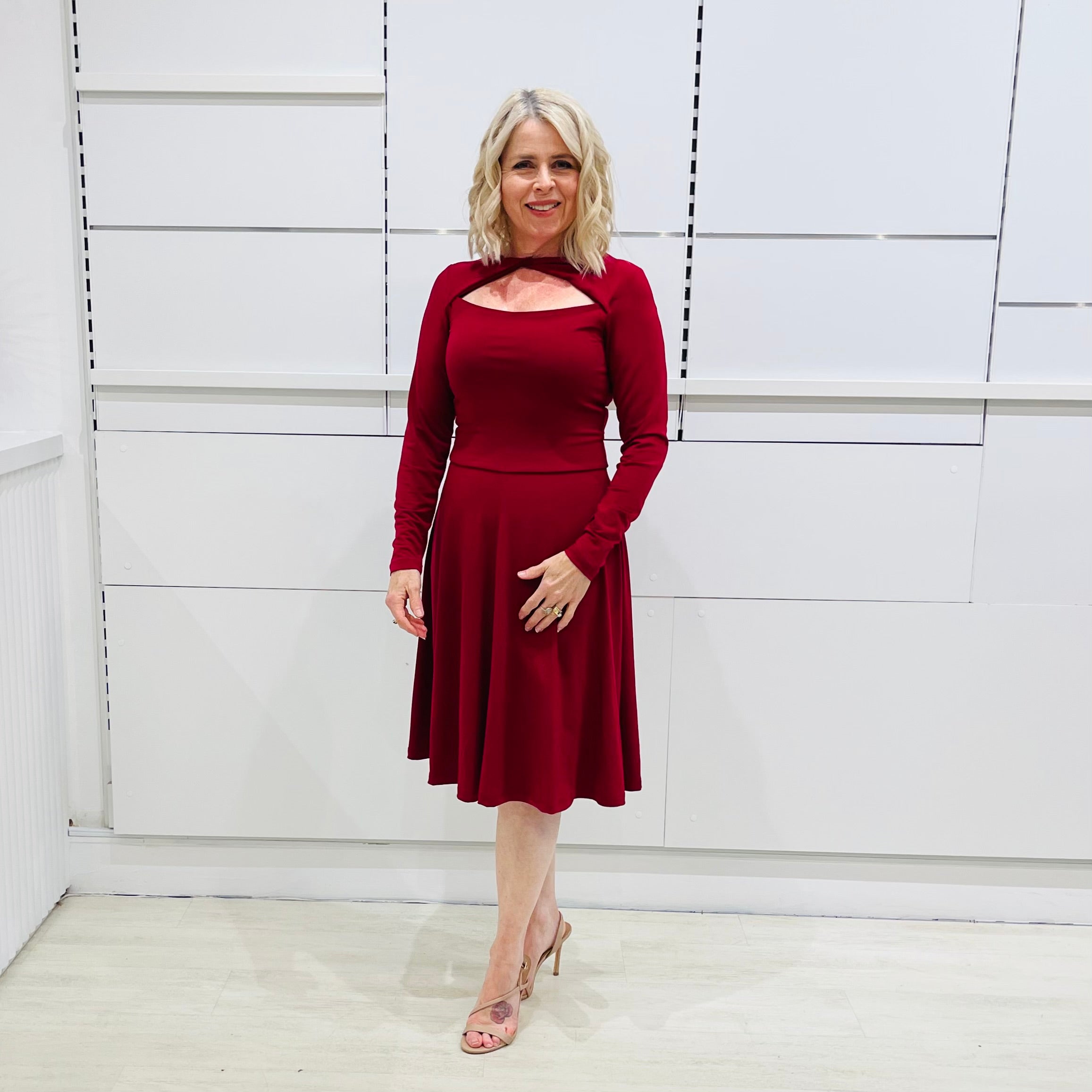 Woman wearing the Penelope dress n rich ruby red, featuring a fit-and-flare, knee length, slihouette, full length sleeves, and a cut out neckline.