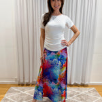 A woman modeling a white short-sleeve top and a vibrant, multicolored floral maxi skirt with blue, red, pink, and yellow tones.