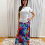 A woman modeling a white short-sleeve top and a vibrant, multicolored floral maxi skirt with blue, red, pink, and yellow tones.