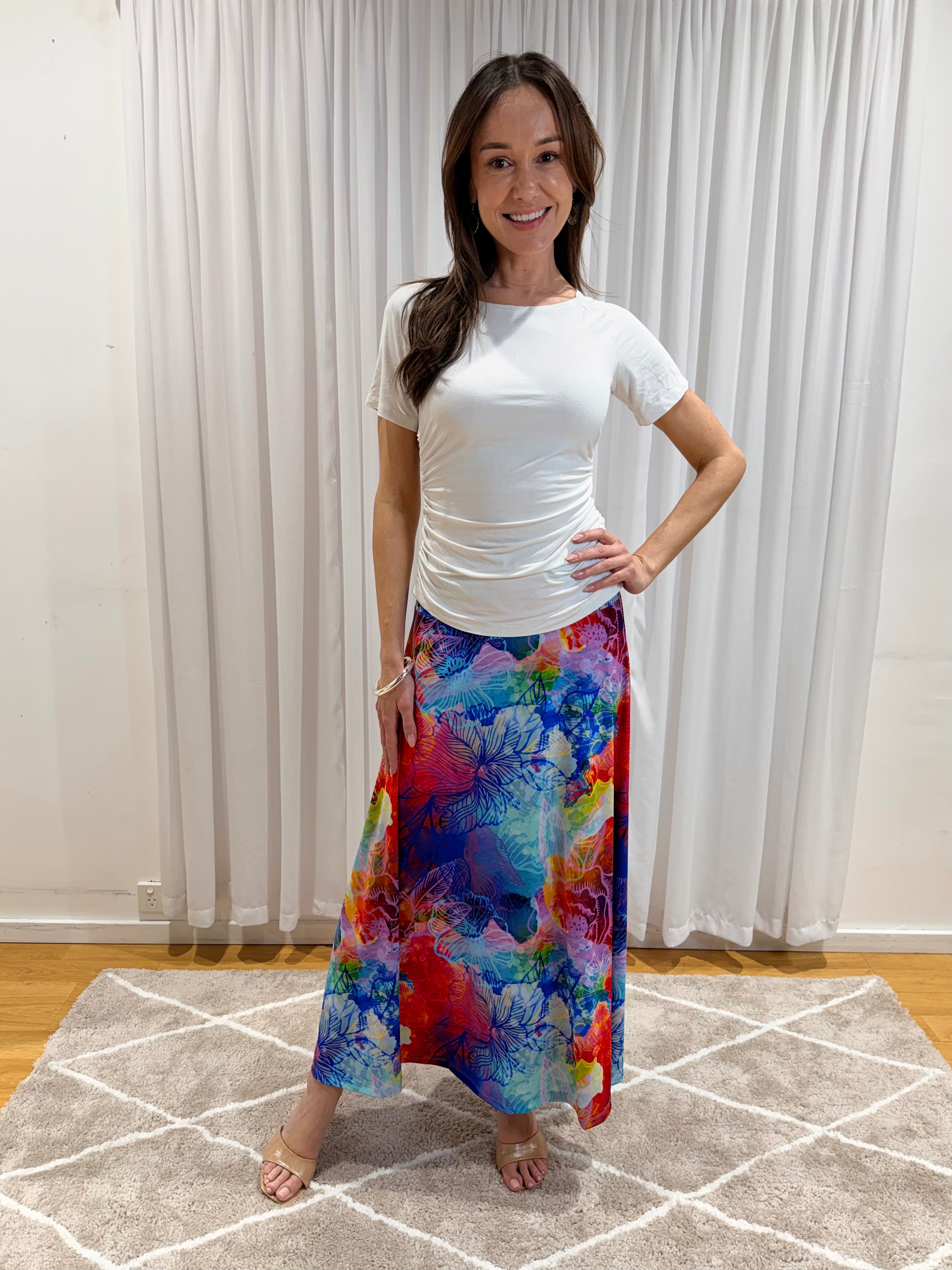 A woman modeling a white short-sleeve top and a vibrant, multicolored floral maxi skirt with blue, red, pink, and yellow tones.