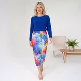 Woman wearing a blue top and colorful skirt in a minimalistic room.