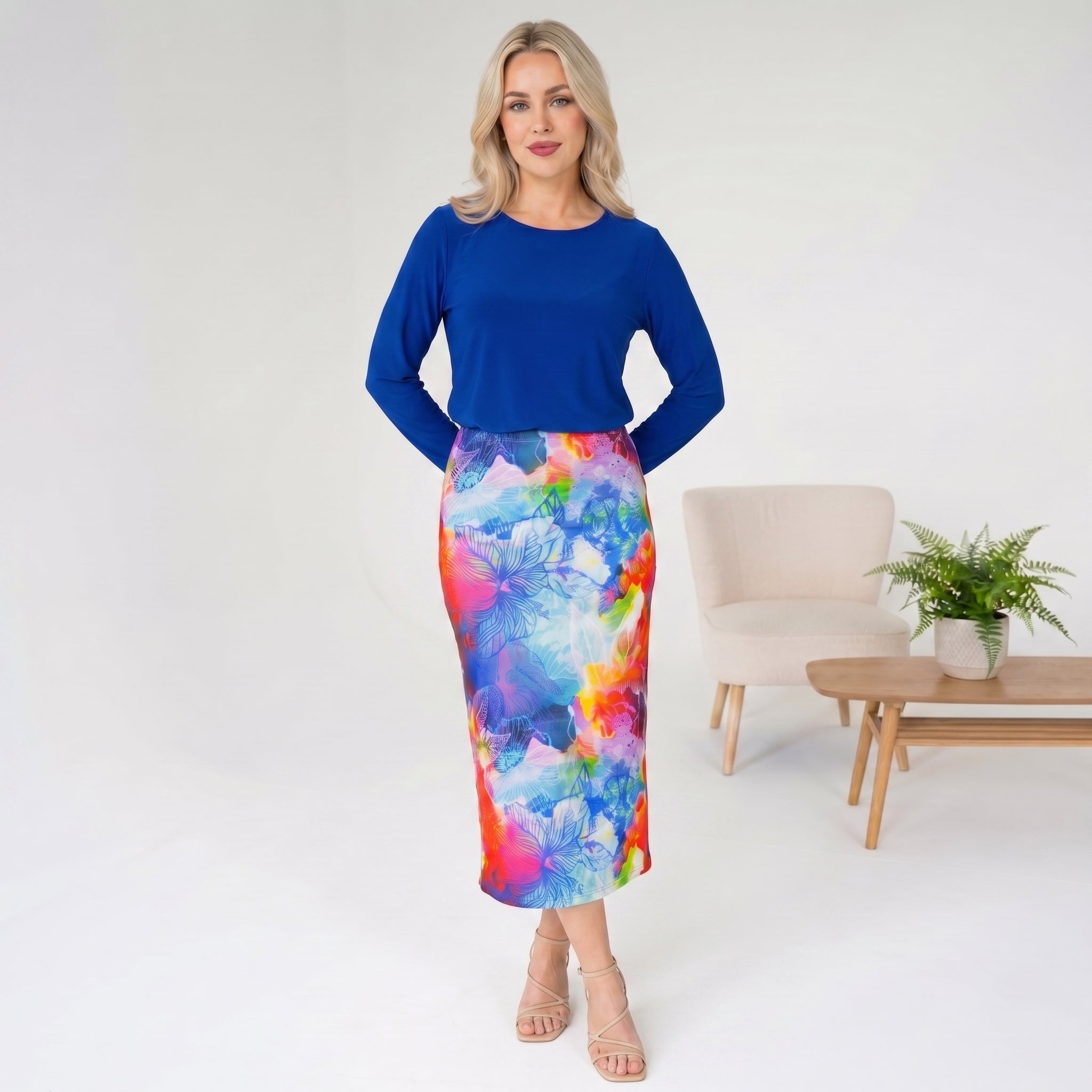 Woman wearing a blue top and colorful skirt in a minimalistic room.