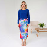 Woman wearing a blue top and colorful skirt in a minimalistic room.