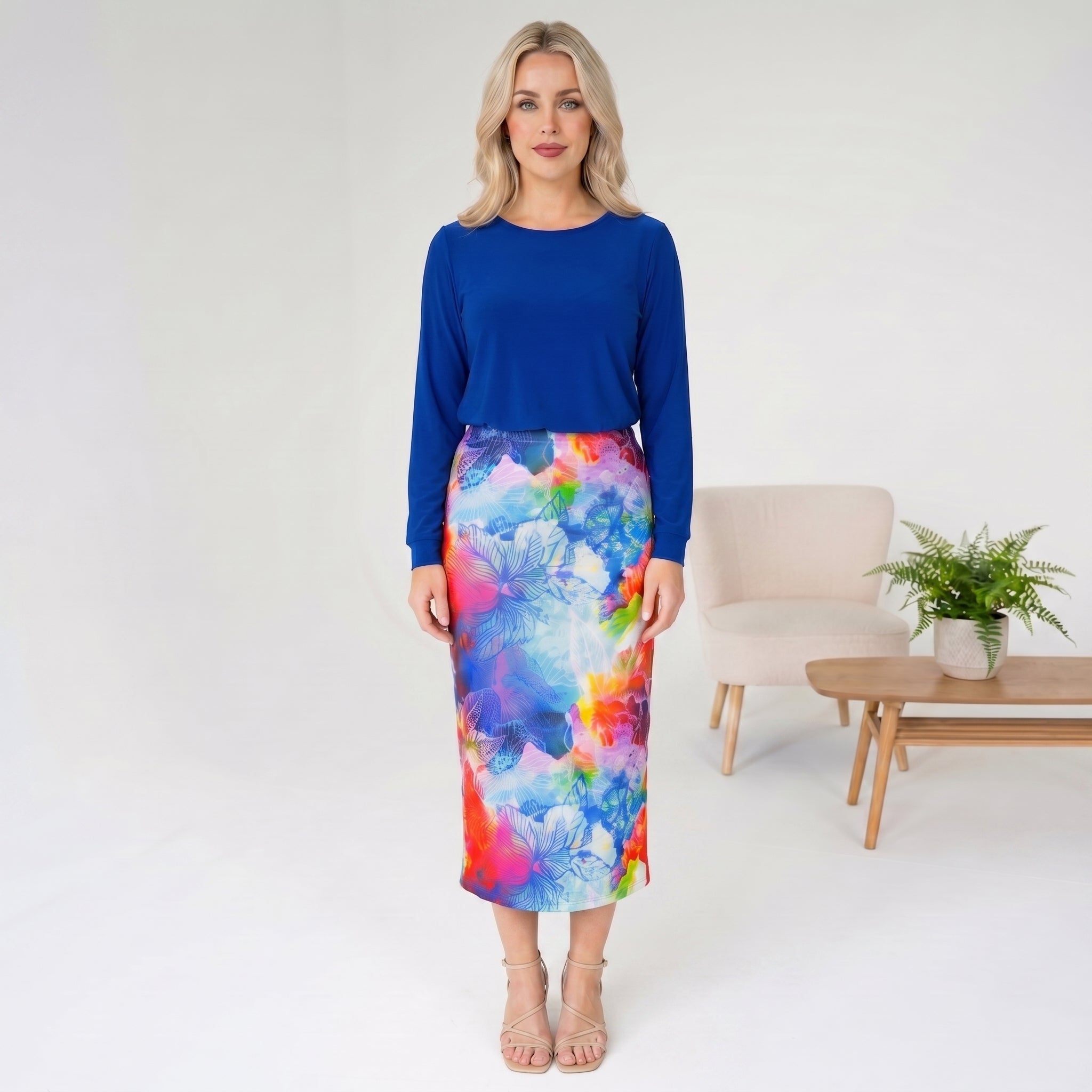 Woman wearing a blue top and colorful skirt in a minimalistic room.