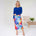 Woman wearing a blue top and colorful skirt in a minimalistic room.