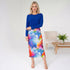 Woman wearing a blue top and colorful skirt in a minimalistic room.