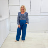 Woman wearing a flowy blue top with a delicate leaf print, scoop neckline, long gathered sleeves, paired with denim blue colored linen pants.