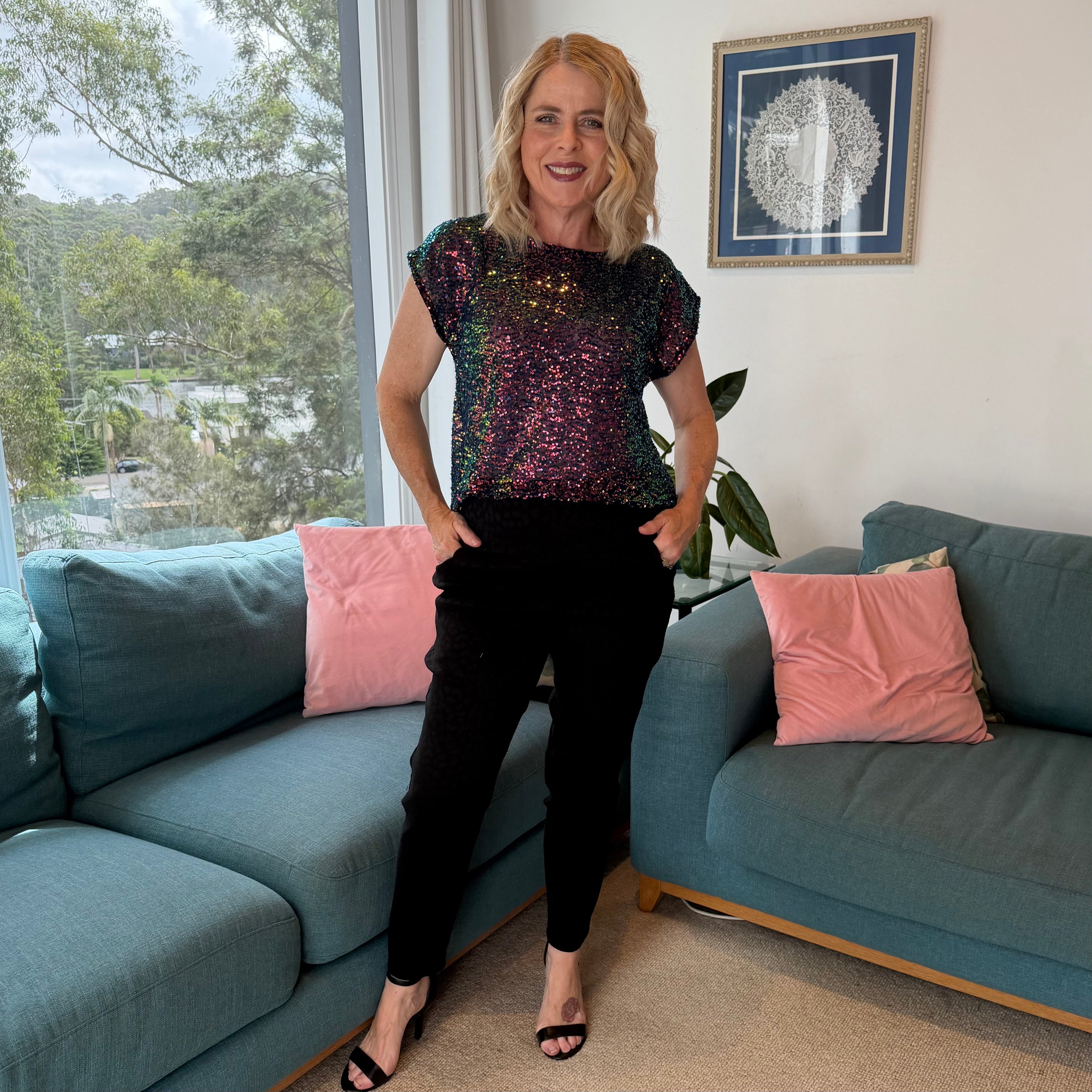 Woman standing in a living room with blue couches and pink pillows.