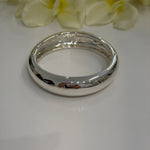 Silver bangle on a white surface with light-colored flowers in the background