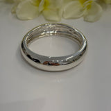 Silver bangle on a white surface with light-colored flowers in the background