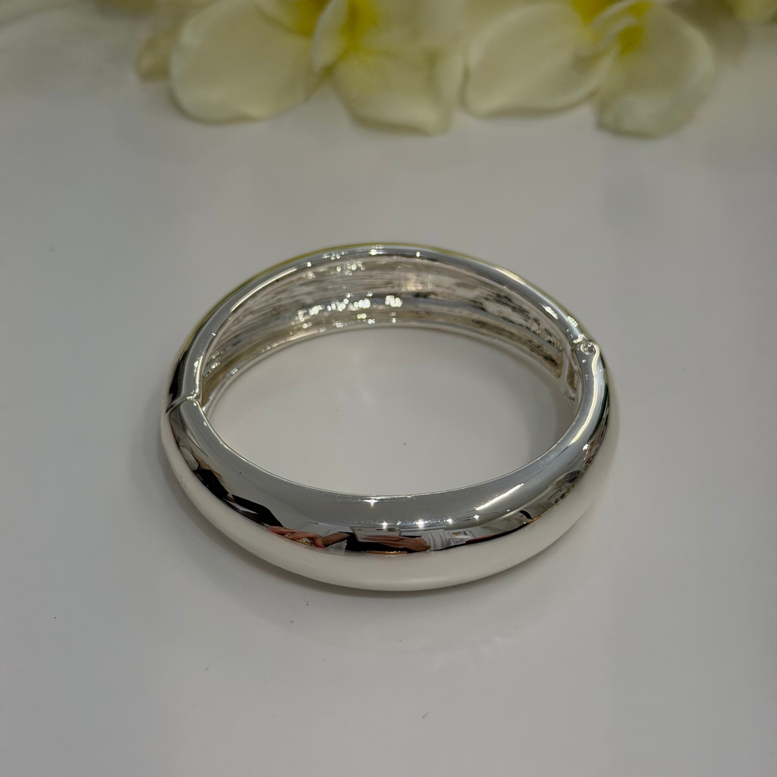 Silver bangle on a white surface with yellow flowers in the background