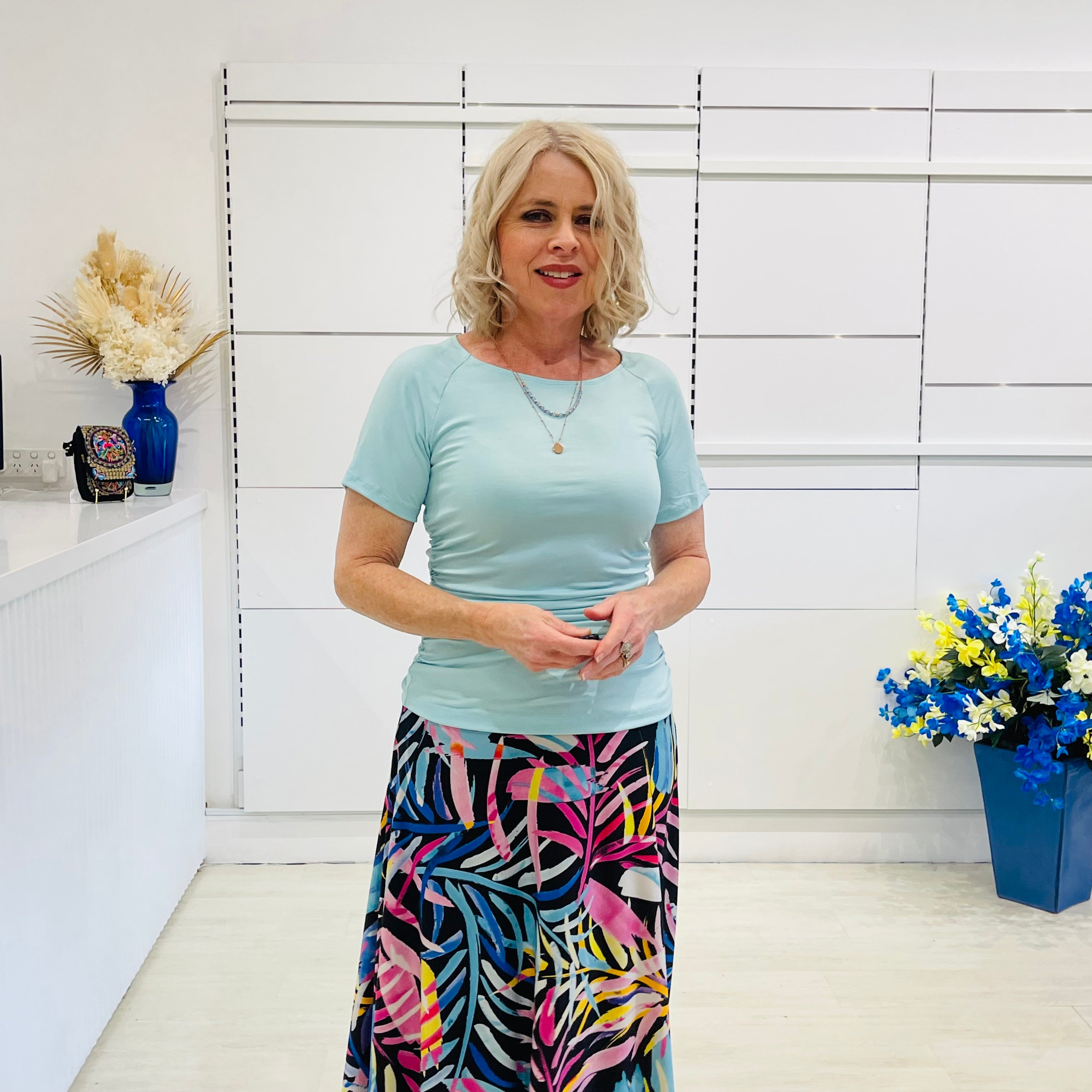 Woman in light green top and colorful skirt standing in a room with white walls and decorative elements.