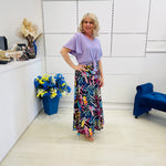 Woman in a colorful skirt and light purple top standing in a modern room with white walls and blue accents.