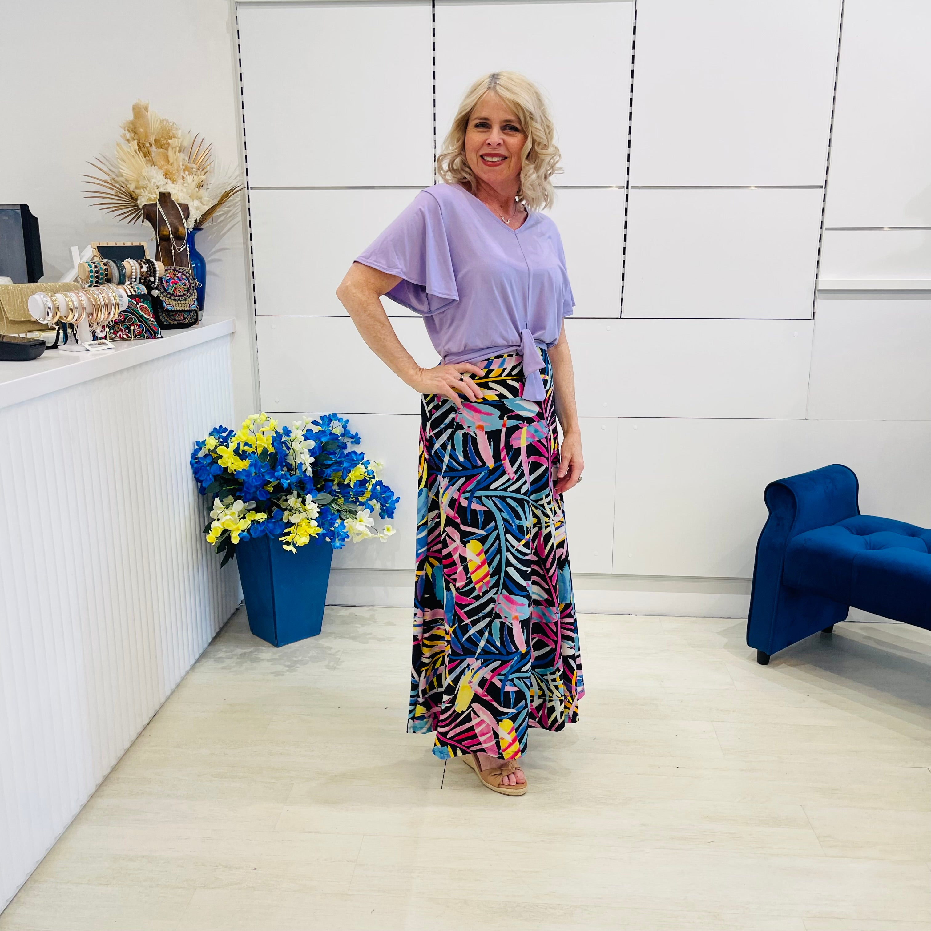 Woman in a colorful skirt and light purple top standing in a modern room with white walls and blue accents.
