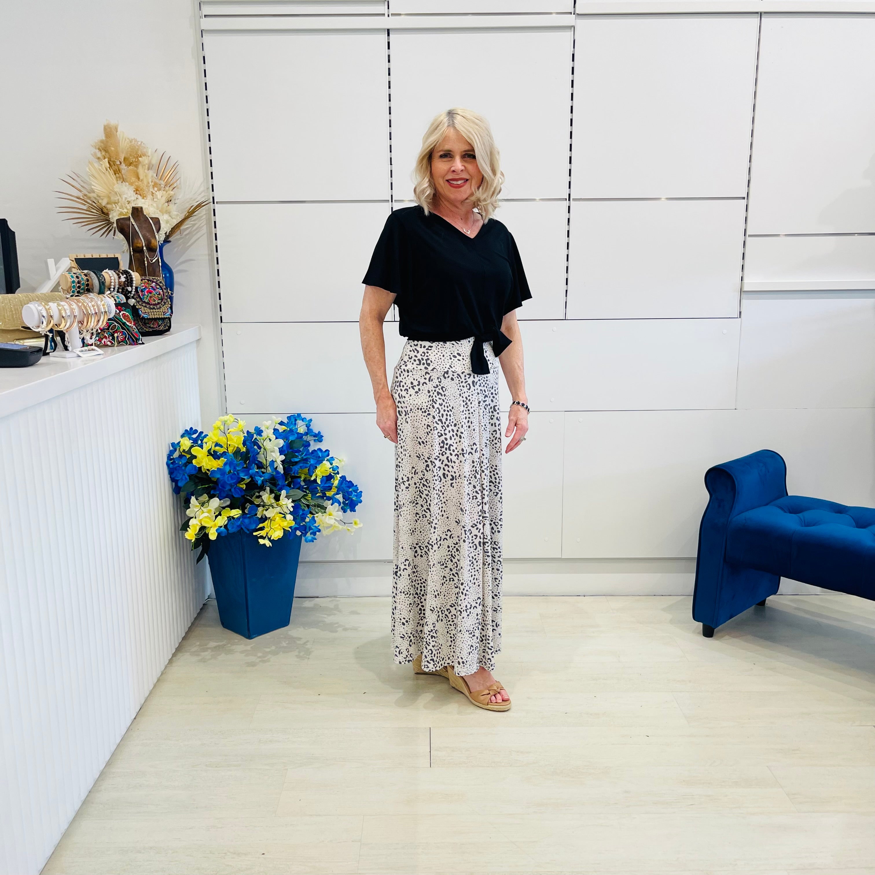 Woman standing in a modern room with a blue couch and floral arrangement.