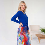 Woman wearing a blue top and colorful skirt in a room with a chair and plant.