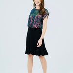 A woman modeling a two-piece outfit consisting of a black flared skirt and a short-sleeve top with a multicolor sequined pattern, set against a plain light gray studio background.