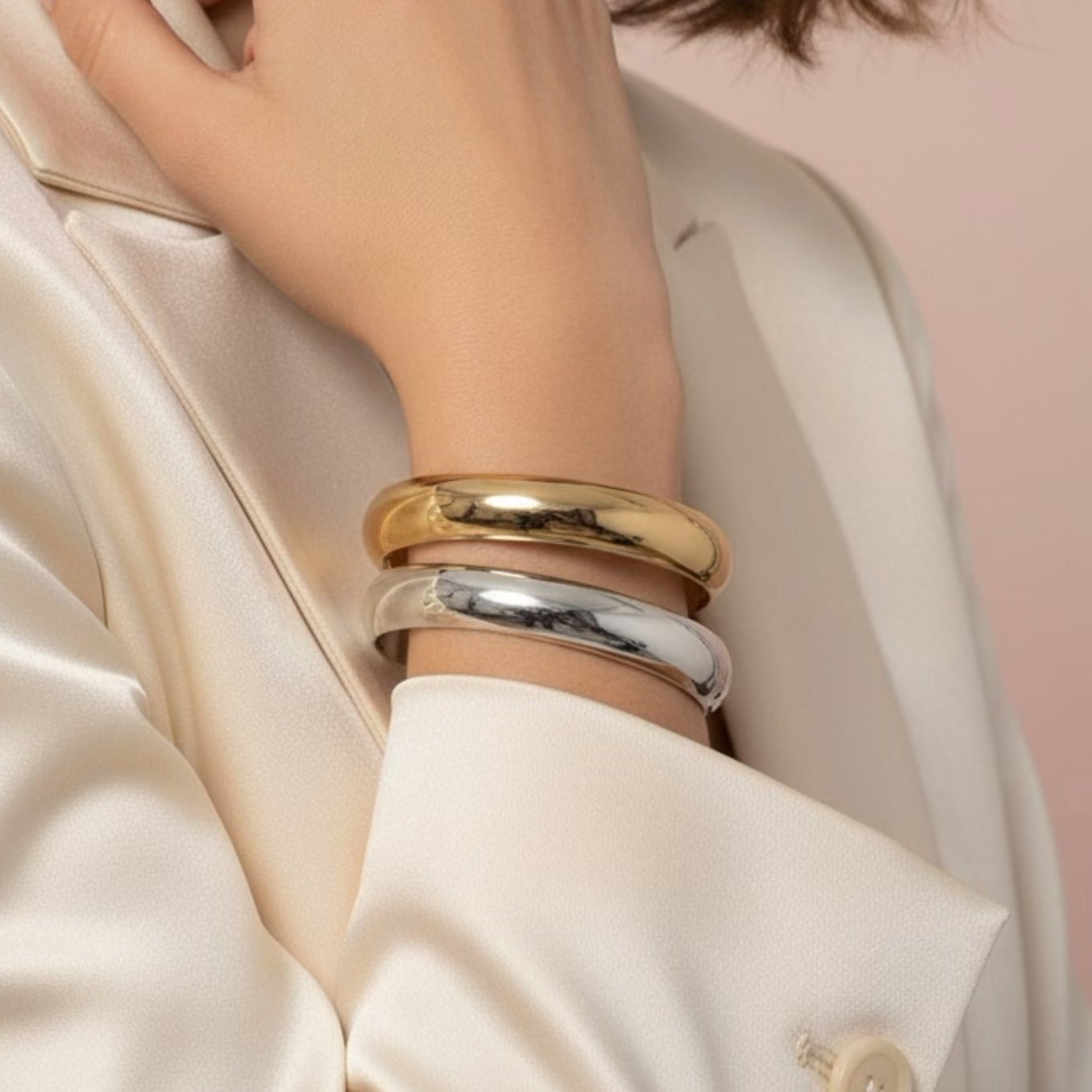 Woman wearing gold and silver bracelets on a pink background
