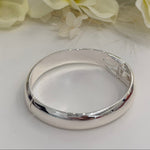 Silver bracelet on a white surface with yellow flowers in the background