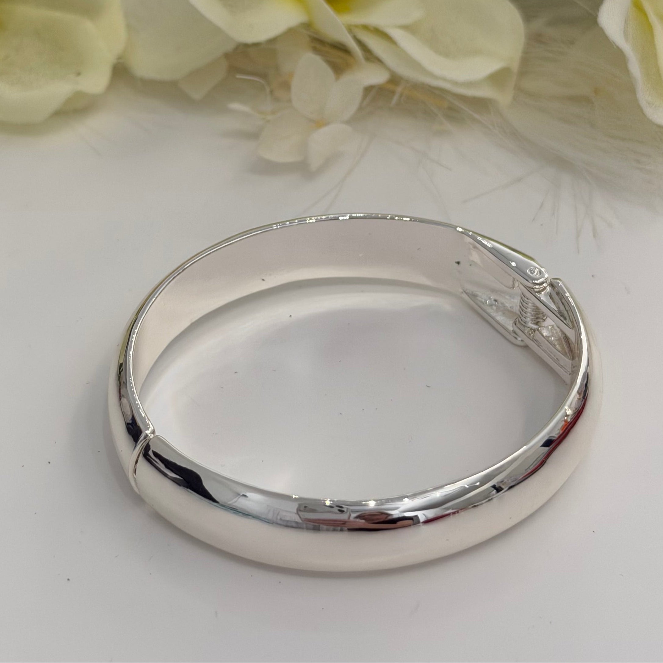Silver bracelet on a white surface with yellow flowers in the background