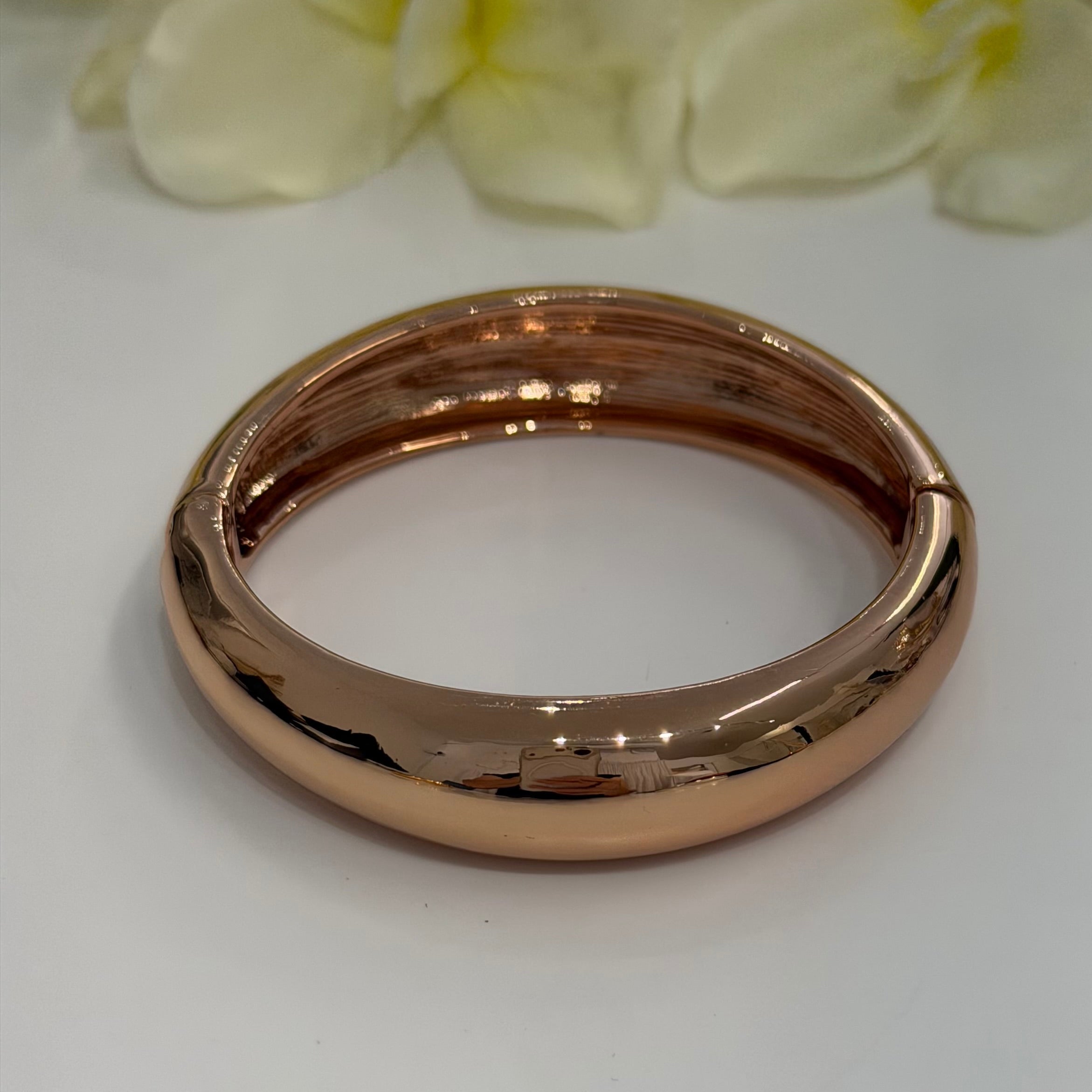Rose gold bangle on a white background with a blurred floral element