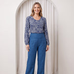 Woman wearing a blue patterned top and blue pants standing in front of a white archway.