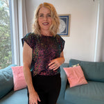 Woman in a sequin top standing in a living room with a couch and pink pillows.