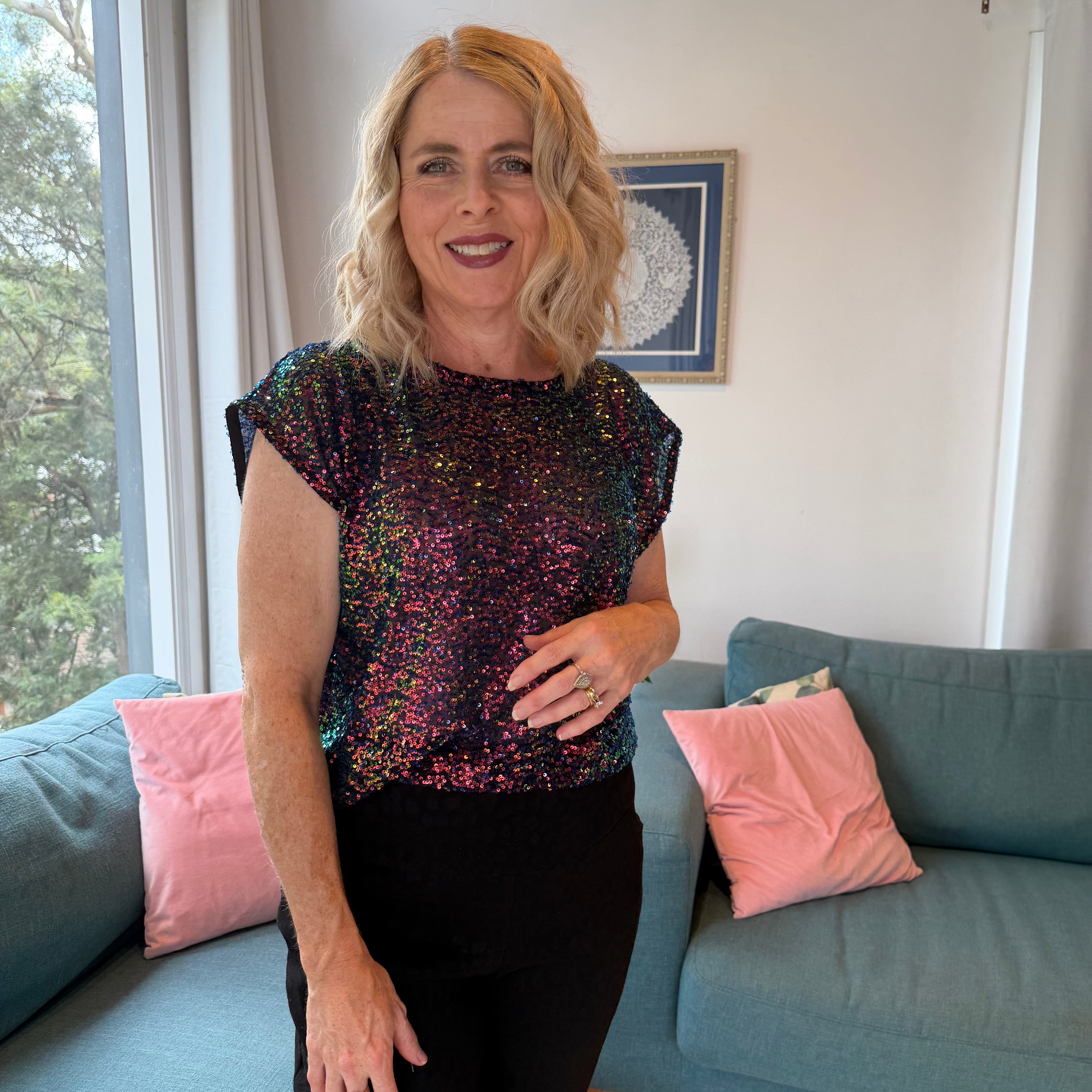 Woman in a sequin top standing in a living room with a couch and pink pillows.
