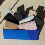 Stack of glittery bags in various colors on a blue box with a wooden surface background