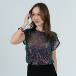 Woman in sparkly top and black skirt in white room 
