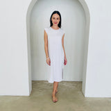 Woman wearing a white dress standing in a minimalistic setting with a white archway.